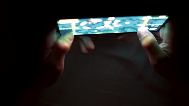 Kind spielt Spiel auf seinem Smartphone im Dunkeln. Hände von Junge und Smartphone vor dunklem Hintergrund — Stockvideo