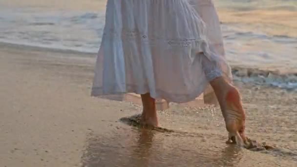 Kvinna bär spets vit kjol långsamt gå barfota den våta sandstranden. Vågor i havet tvätta stranden — Stockvideo