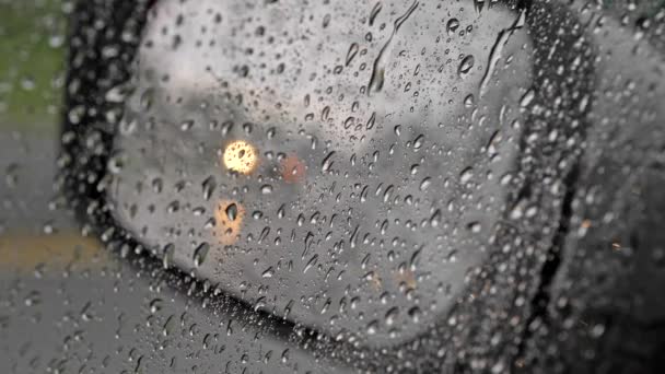 Gotas de lluvia en una ventana lateral de un coche. Luces borrosas de paso por los coches reflejándose en un espejo retrovisor. Gotas de agua deslizándose por la superficie de vidrio. Vista desde el interior del coche, UHD — Vídeo de stock