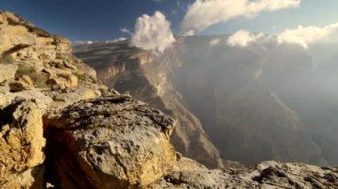 Jebel Shams Dağı, Umman. Yakın kısımda büyük sarı taşlar ve uzak kısımda sis var. Güzel beyaz bulutlar dağa dokunuyor. Turna steadicam shot, 4k