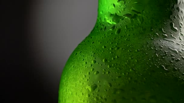 Botella de cerveza verde cubierta con gotas de agua girando sobre fondo oscuro. Primer plano, UHD — Vídeo de stock