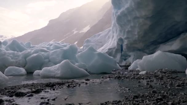 Derretimiento del glaciar por una montaña en Noruega. Trozos de nieve congelada yaciendo en el suelo derritiéndose. El agua fluye por el suelo. Grúa tiro, UHD — Vídeos de Stock