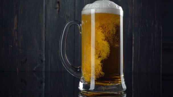 Spowolnione ujęcie piwa wlewającego się do kubka piwa. Biała piana piwna wychodzi poza krawędzie kubka. Starzejące się drewniane tło — Wideo stockowe