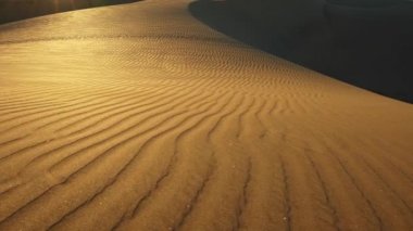 Gün batımında bir deseni olan kum tepeciği çölde güneş ışınları saçar. Kum taneleri parçalanıyor. Kamera yana hareket ediyor. UHD