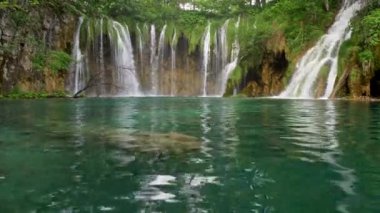 Hırvatistan 'ın Plitvice Lakes Ulusal Parkı' ndaki turkuaz renkli şeffaf göl suları. Arka planda şelaleler ve şelaleler. UHD