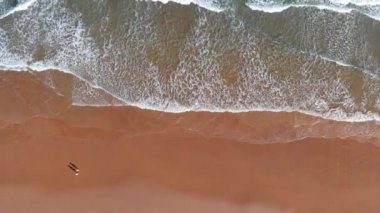 Kuzey İspanya. Okyanus kumsalında uçuyor. Issız plajda yürüyen bir çift insan. Yukarıdan aşağısı, 4K.