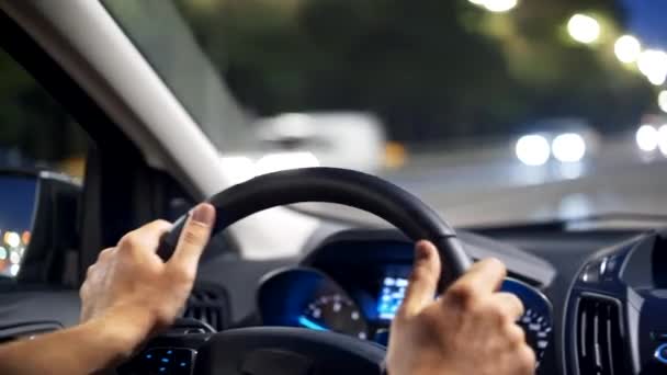 Um homem a conduzir um carro na cidade da noite. Mãos masculinas segurando o volante. Tráfego. 4K — Vídeo de Stock