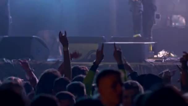 Het publiek van jonge mensen springen met hun handen vertonen teken van hoorns gebaar en dansen in ritme van de muziek tijdens rockconcert. 4K — Stockvideo