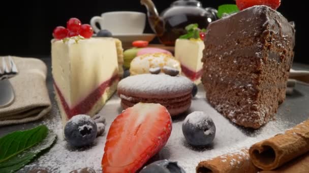 Variety of cakes with fruits. Cheese cake, chocolate cake and cream puff cake. Strawberry and mint topping. Sliding probe shot of set delicious dessert home made cakes over dark background. UHD, 4K — Stock Video