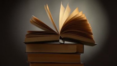 Yavaş çekimde kitap rüzgarda sallanıyor. Siyah arkaplan üzerine kitap yığını