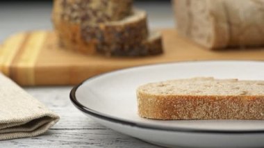 Kadın eli ekmeğe tereyağı sürüyor. Tereyağlı ekmek. Arka planda dilimlenmiş ekmek UHD, 4K