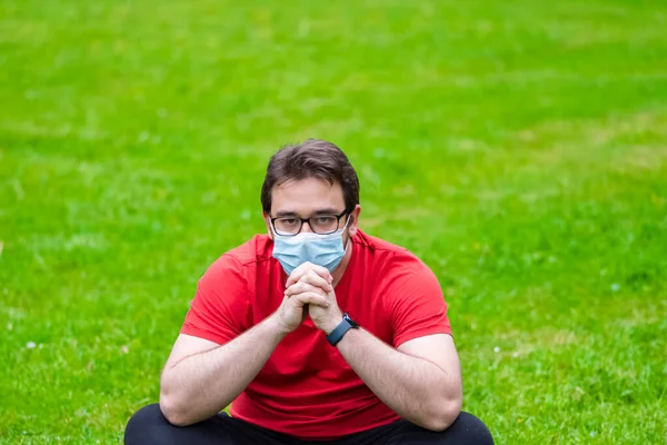 Egzersizden sonra dinlenmek için çimlerin üzerinde oturan Corona 'ya karşı önlem almak için yüz maskesi takan şişman bir adam.