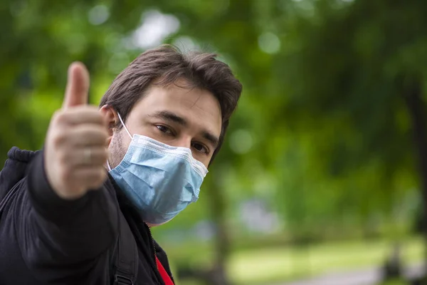Corona virüsü salgınına karşı alınan önlemleri takip eden cerrahi maske takan adam işaret veriyor, baş parmak yukarı, parmak yukarı Corona ile yeni yaşam tarzında pozitif kalmaya devam ediyor.