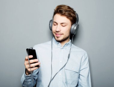 Kulaklık takan ve cep telefonu tutan genç bir adam.