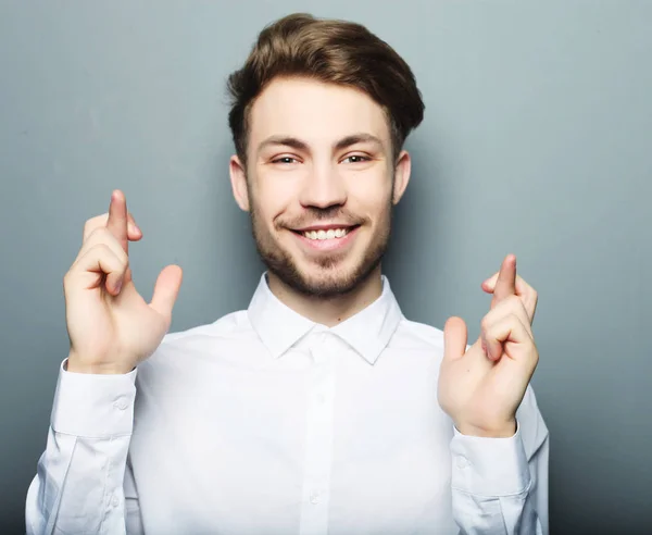 Young man in shirt keeping fingers crossed while standing agains — Stock Photo, Image