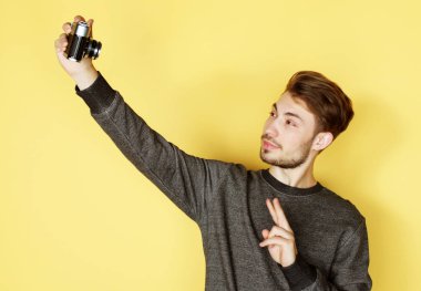 Gülümseyen adam sarı arka planda selfie çekiyor.
