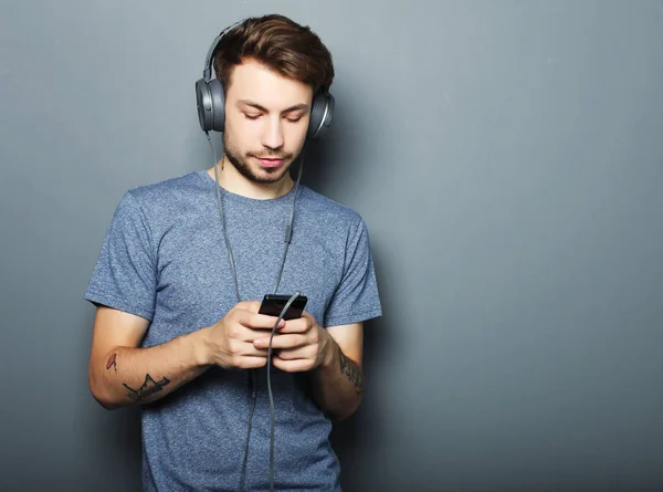 Joven usando auriculares y sosteniendo el teléfono móvil — Foto de Stock