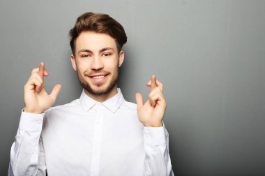 Tişörtlü genç adam ayaktayken parmaklarını çapraz tutuyor.