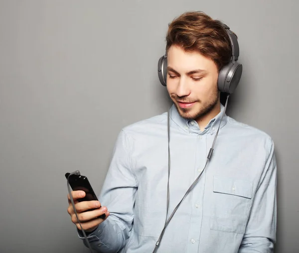 Homem jovem usando fones de ouvido e segurando telefone celular — Fotografia de Stock