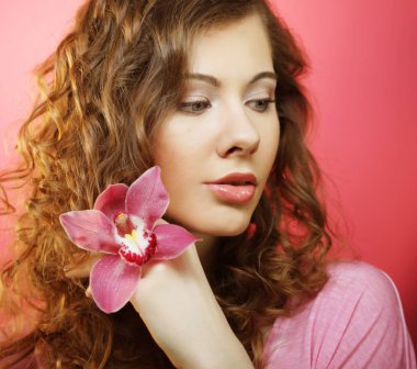 Pembe arka planda orkide çiçeğiyle güzel mutlu bir kadın.