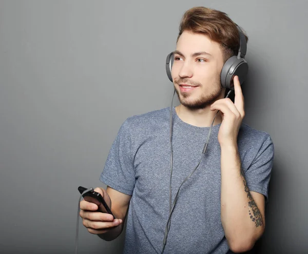 Joven usando auriculares y sosteniendo el teléfono móvil — Foto de Stock