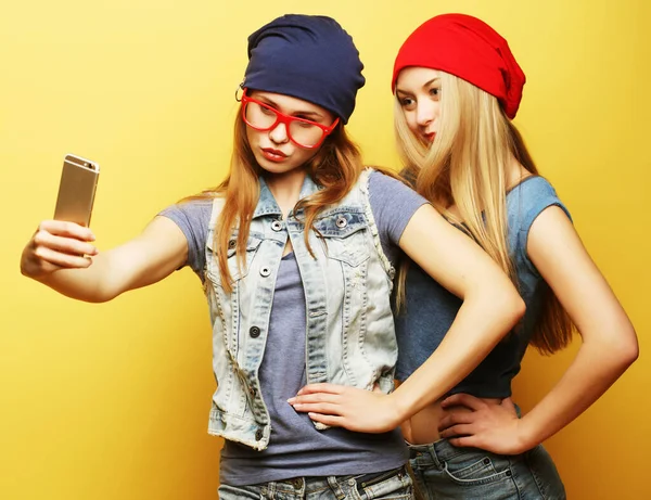 Dos jóvenes amigas hipster tomando selfie sobre fondo amarillo —  Fotos de Stock