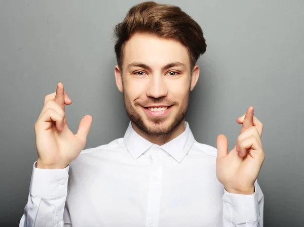 Young man in shirt keeping fingers crossed while standing agains — Stock Photo, Image