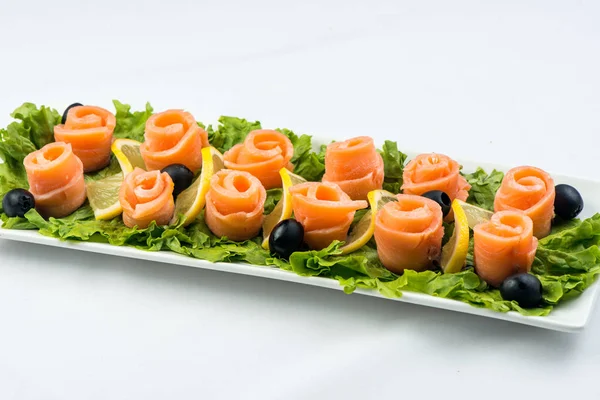 Salmon snack on lettuce leaf with lemon and olives on white plate on white background — Stock Photo, Image