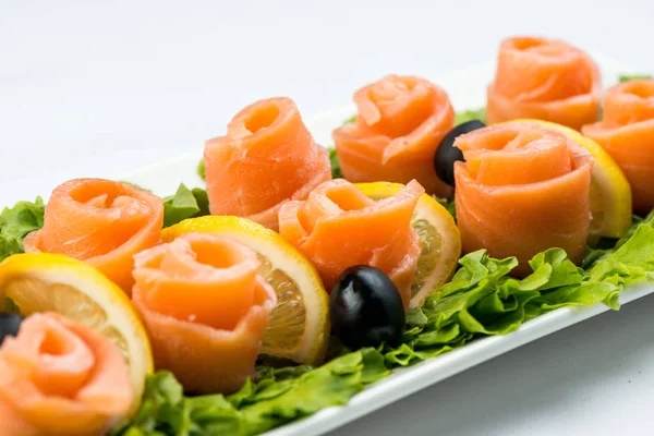 在白色背景上白色盘子上的柠檬和橄榄的生菜叶上的鲑鱼小吃 — 图库照片