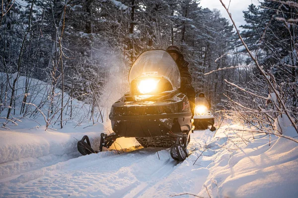 Moto de nieve por la noche pasa por el bosque de invierno. faros. carretera nocturna a través del bosque de invierno. moto de nieve por la noche — Foto de Stock
