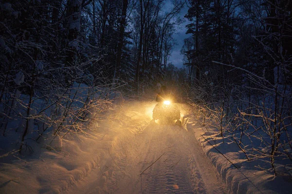 Mit dem Motorschlitten geht es abends durch den Winterwald. Scheinwerfer. Nachtstraße durch den Winterwald. Schneemobil in der Nacht — Stockfoto