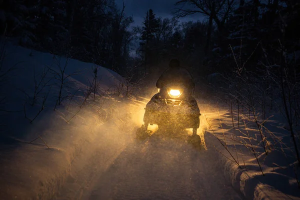 Snowmobile in the evening goes through the winter forest. headlights. night road through the winter forest. snowmobile at night — Stock Photo, Image