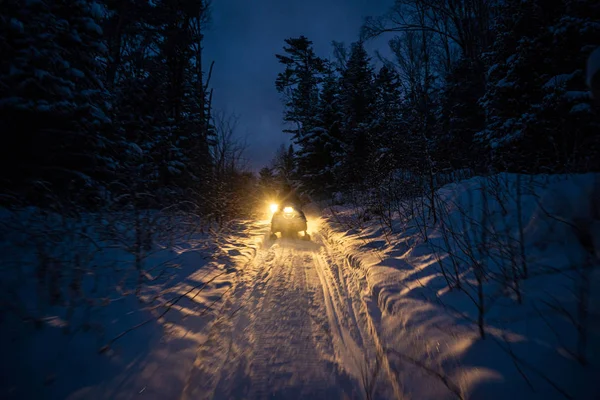Snowmobile in the evening goes through the winter forest. headlights. night road through the winter forest. snowmobile at night — Stock Photo, Image