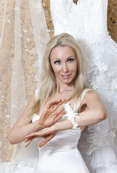 Die Braut, die junge Frau mit den blonden langen Haaren und dem Strumpfband in der Hand träumt von einer Hochzeit in der Nähe eines Brautkleides — Stockfoto