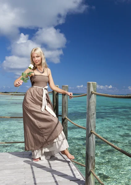 De mooie vrouw in een lange jurk op een houten platform over de zee — Stockfoto