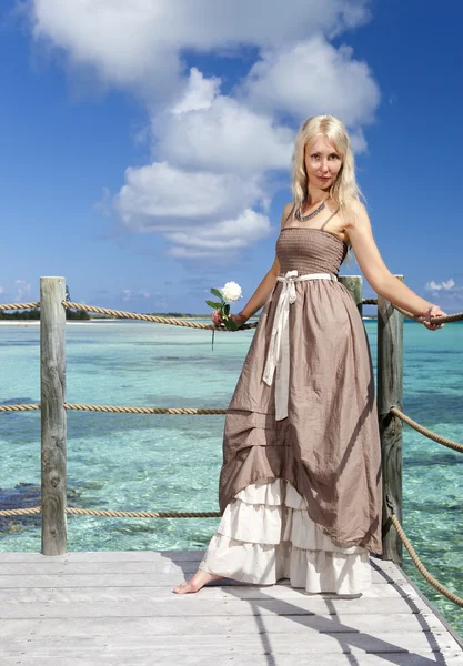 Denizin üzerinde ahşap bir platformda uzun elbiseli güzel kadın — Stok fotoğraf