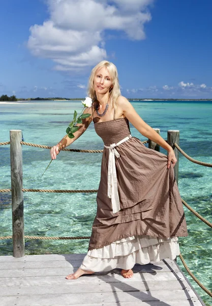 Die schöne Frau in einem langen Kleid auf einer Holzplattform über dem Meer — Stockfoto