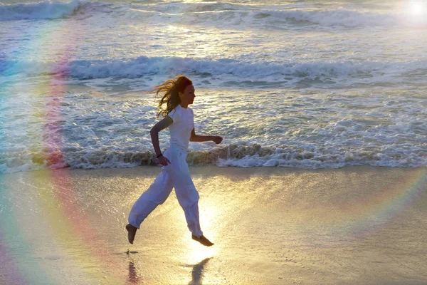 Silhueta de mulher correndo ao longo da borda do mar em um pôr do sol — Fotografia de Stock