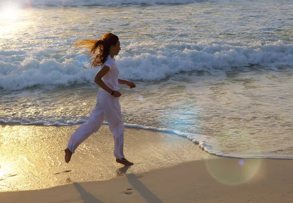 Силует жінки, що біжить уздовж краю моря на заході сонця — стокове фото