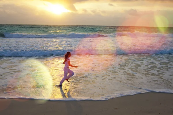 Silhueta de mulher correndo ao longo da borda do mar em um pôr do sol — Fotografia de Stock