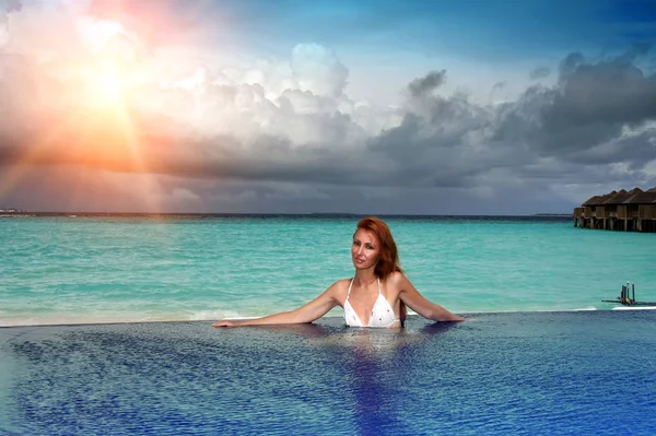 A jovem mulher bonita na piscina antes do mar ao pôr do sol — Fotografia de Stock