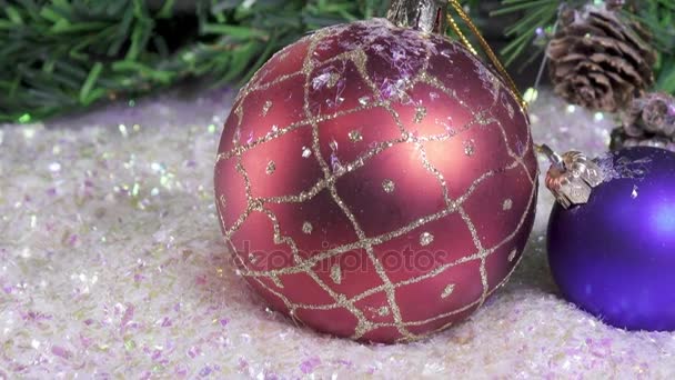 New Years balls lie on snow against the background of a Christmas fir-tree — Stock Video