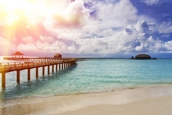 Maldivas. O mar azul-turquesa ao sol e a ponte de madeira sobre a água — Fotografia de Stock