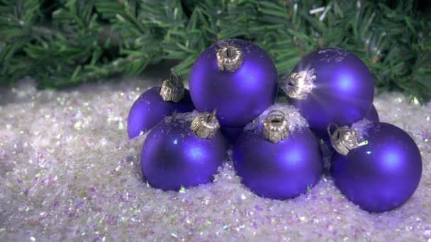 Сніг повільно падає на новорічні кульки на тлі ялинки — стокове відео