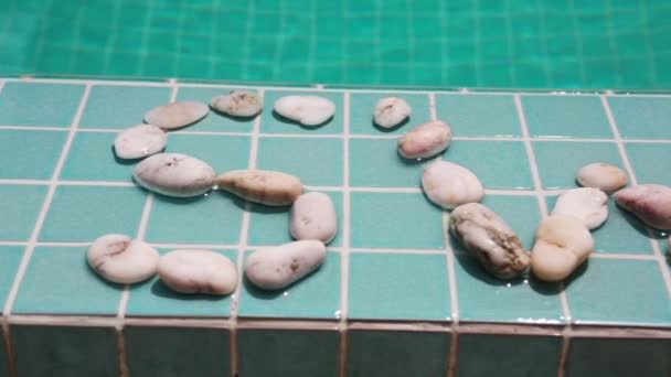 Inskriptionen "simma" är anlagd av sten på en pool sida — Stockvideo