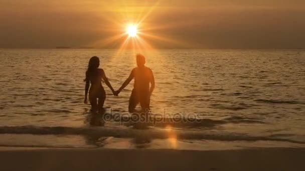 Siluetas del hombre y la mujer, dejando el mar al atardecer — Vídeos de Stock