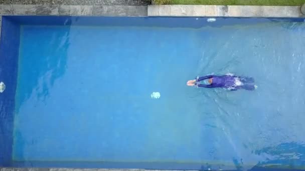 Привлекательная женщина в мусульманском купальнике буркини брызгает водой в бассейн и плавает — стоковое видео