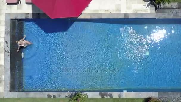 De mooie jonge vrouw zwemt in het zwembad in een tropische tuin, luchtfoto van drone — Stockvideo