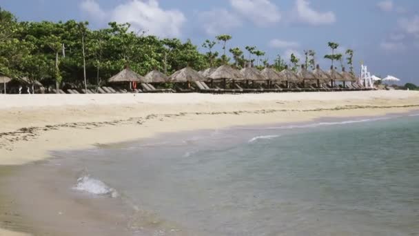 Olas del mar caliente corren en la playa de arena del complejo tropical con sombrillas y tumbonas — Vídeos de Stock