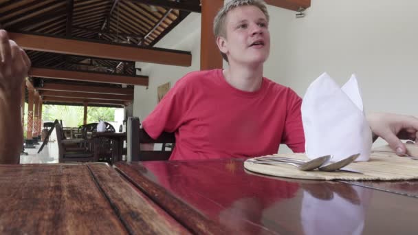Молодой человек ждет заказа в ресторане и общается с друзьями — стоковое видео